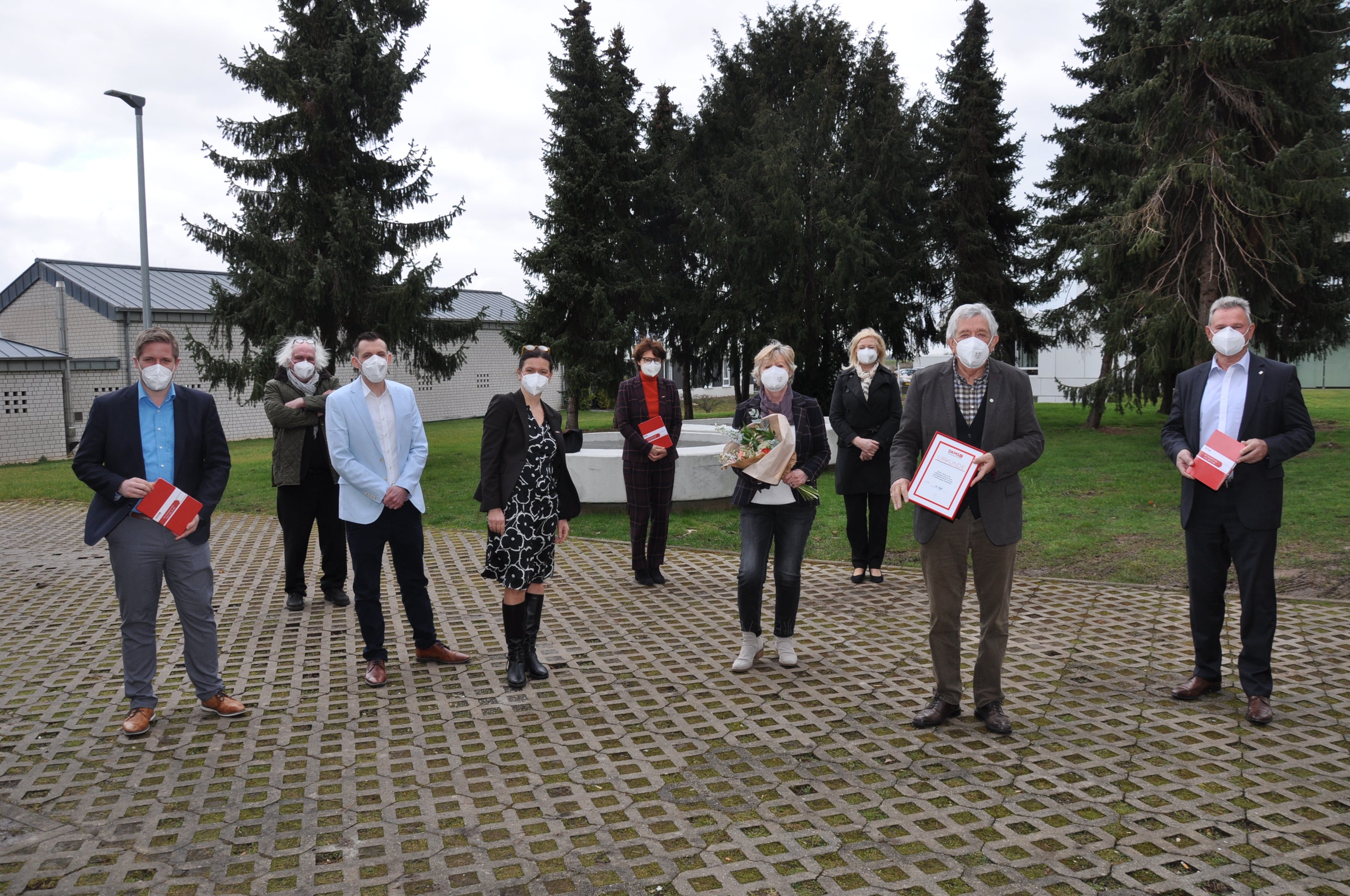 Scheckübergabe von 100.000 Euro der Hilfsgruppe Eifel an die DKMS, die Gruppe steht mit Masken und Abständen auf einer Fläche