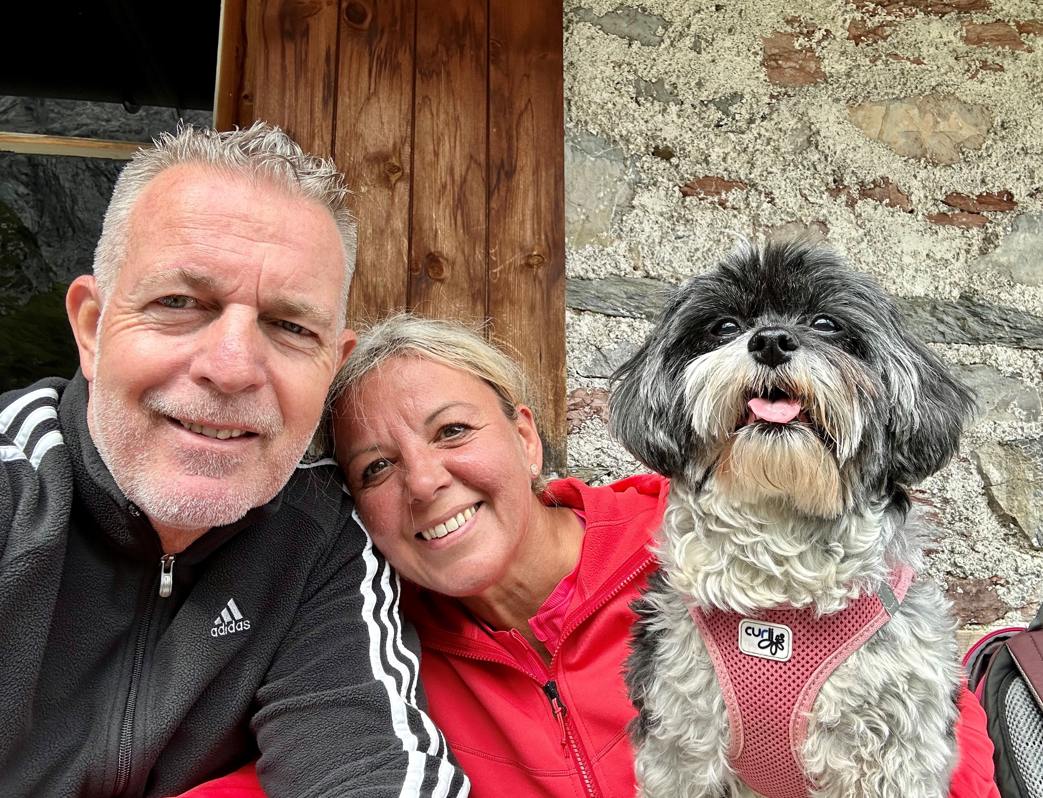 Ein Mann und eine Frau sind fröhlich vor einer Hauswand mit einem Hund