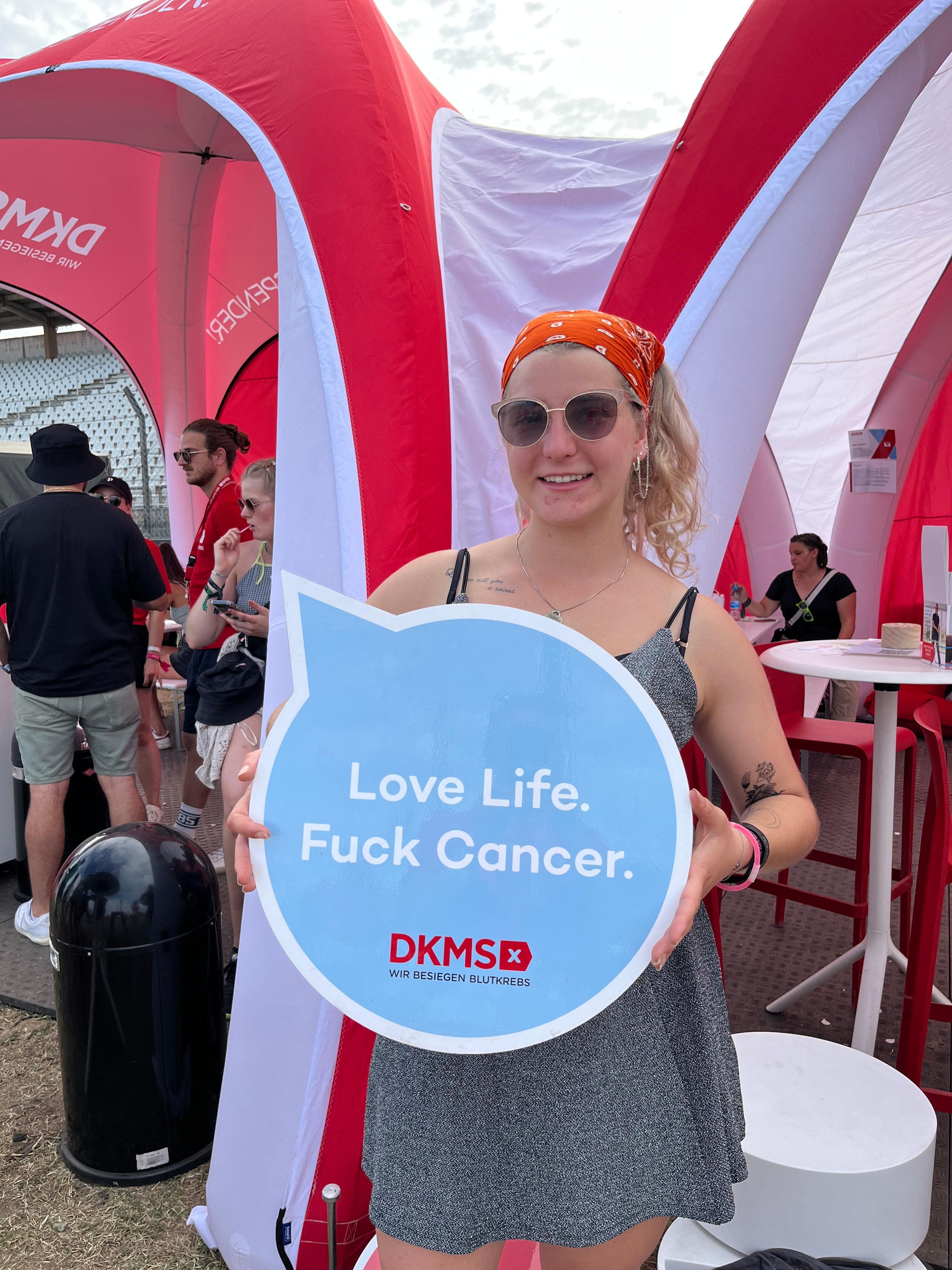 Eine Frau hält ein Schild mit der Aufschrift: Love Life. Fuck Cancer.