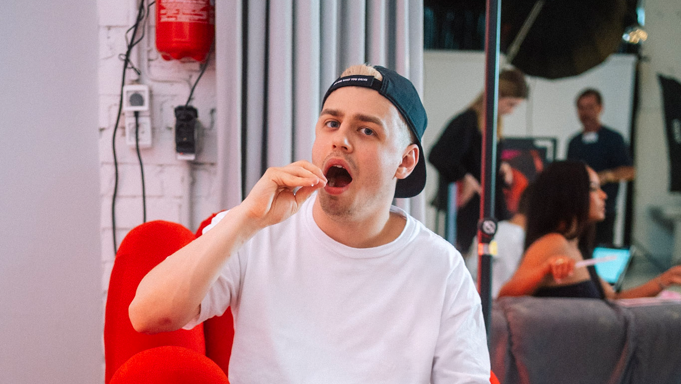 Papaplatte der mit einem Wattestäbchen einen Wangenabstrich macht und Hintergrund drei Personen an einem Set stehen. 