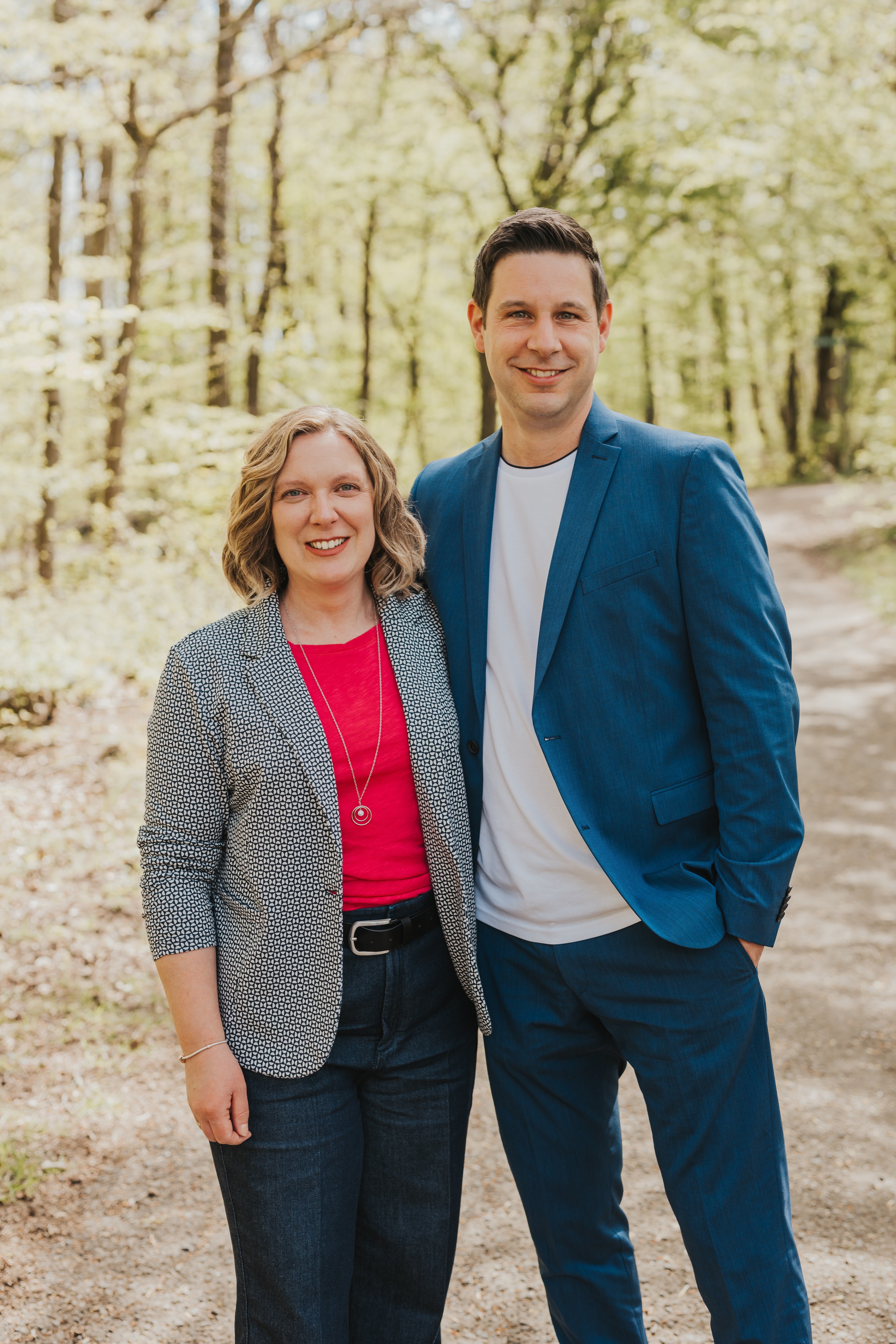 Christoph und seine Ehefrau stehen Arm in Arm in einem Wald und lächeln in die Kamera.