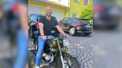 Ein Mann sitzt in T-Shirt und Jeans auf einem Motorrad.