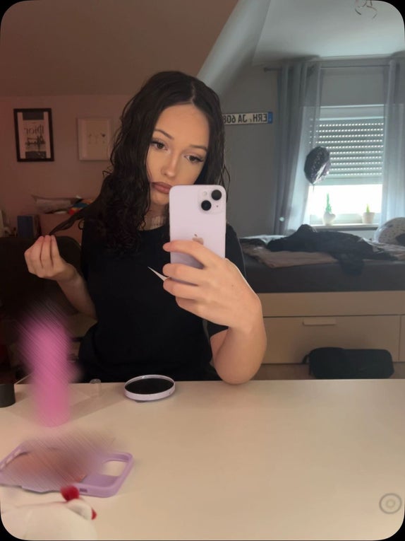 Eine junge Frau macht ein Foto mit ihrem Handy. Sie hat lange dunkle Haare und trägt ein schwarzes T-Shirt.