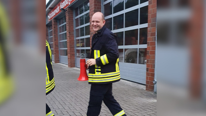 Ein Mann trägt eine Feuerwehruniform und hält ein rotes Megafon. 