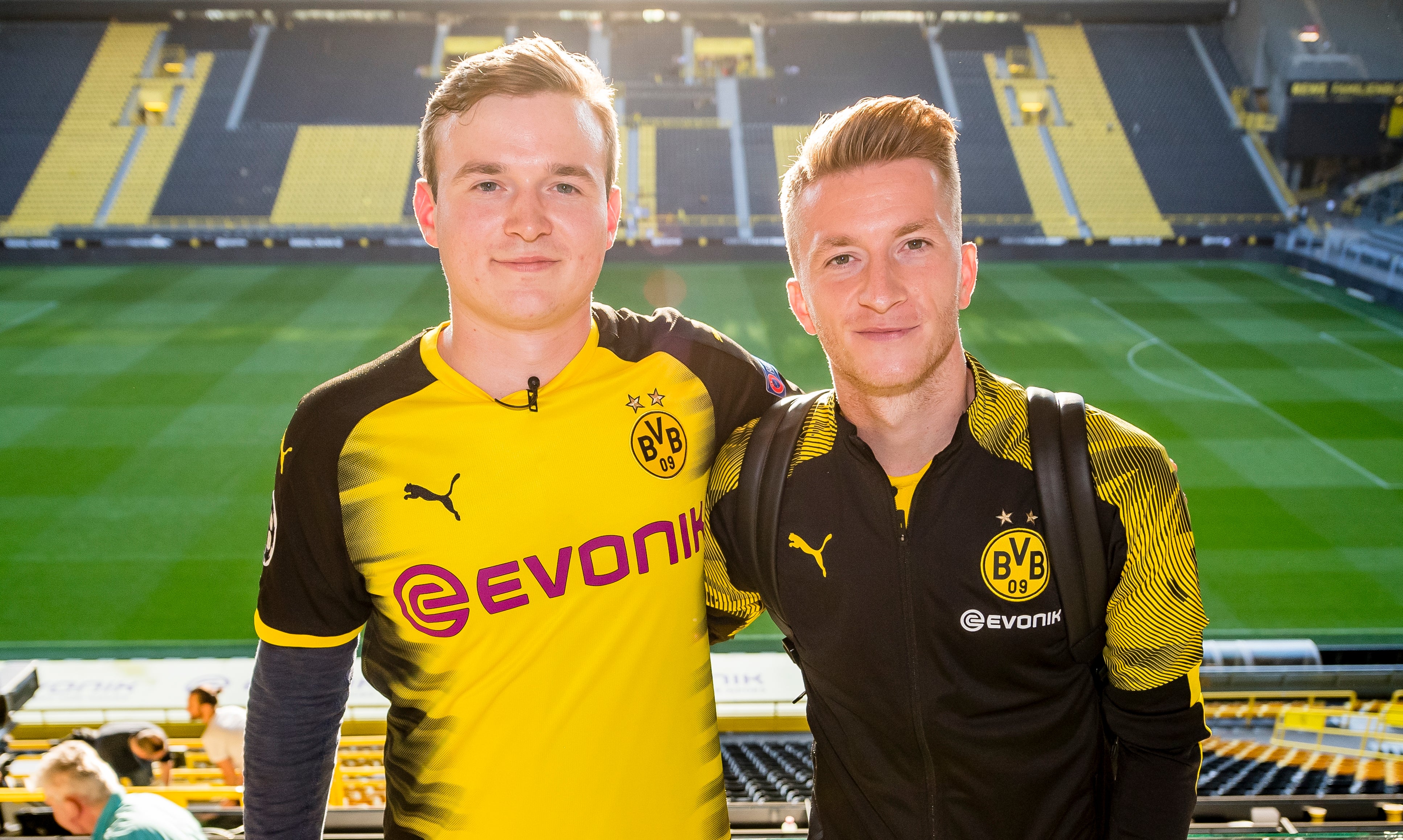 Ludwig Jolmes und Marco Reus, beide tragen BVB Merch und im Hintergrund sieht man das BVB Stadion