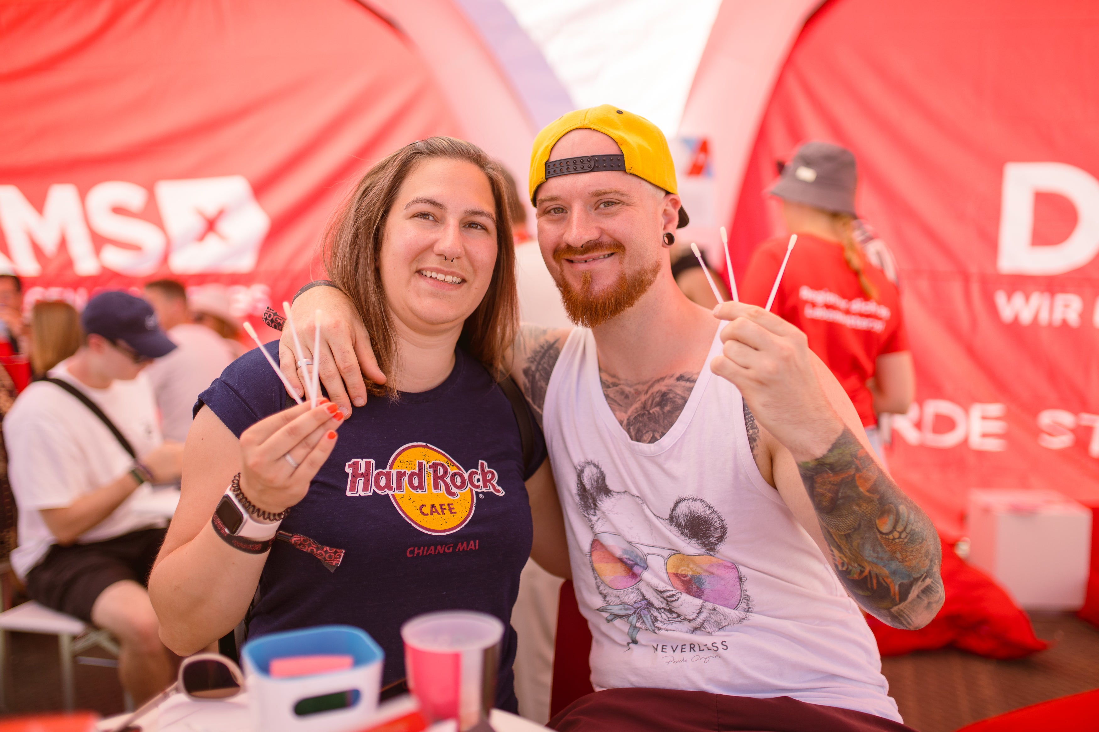 Ein Mann und eine Frau halten Wattestäbchen hoch, im Hintergrund sieht man das DKMS Logo
