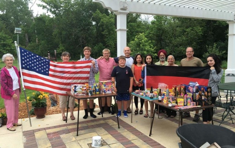 Eine Gruppe von Menschen posiert für ein Foto. Die Personen links halten eine Flagge der Vereinigten Staaten. Die Personen rechts halten eine Deutsche Flagge.