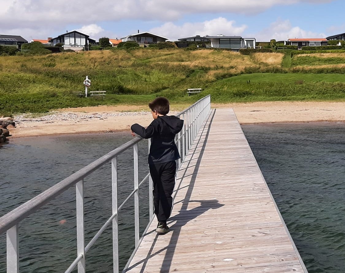 ein Junge steht auf einem Steg der Richtung Strand führt