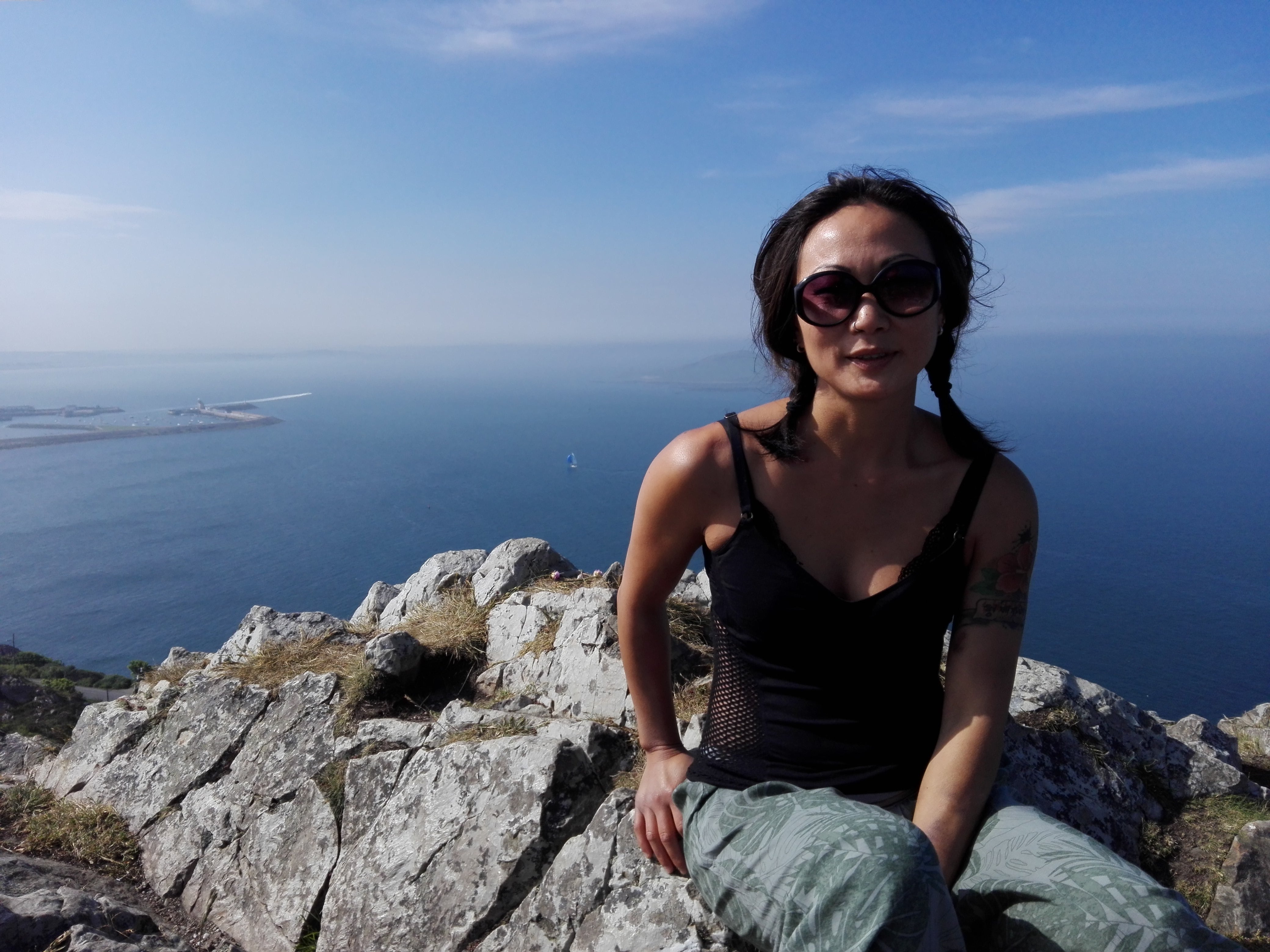 Patientin Madeleine sitzt auf einem Felsen mit dem Rücken zum Meer.