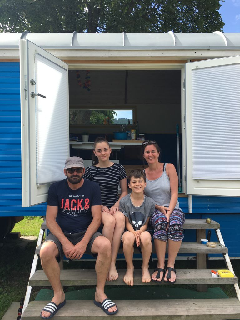 Mattes und seine Familie, die in einer Tür eines blau-weißen Wohnwagens sitzen