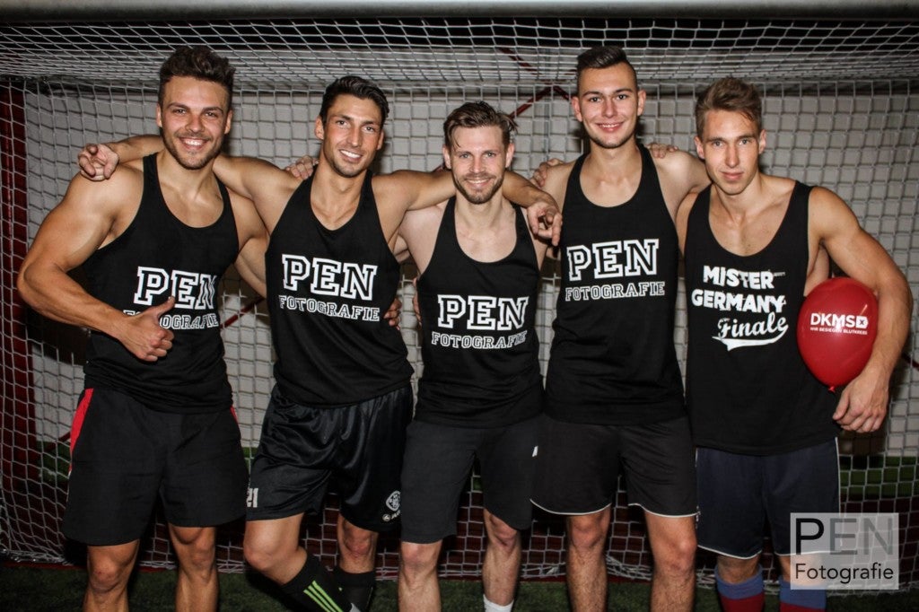 Eine Gruppe von Männern in schwarzen Trägerhemden posieren vor einem Spieltor. 