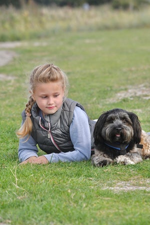 Ein Mädchen liegt im Gras neben einem Hund