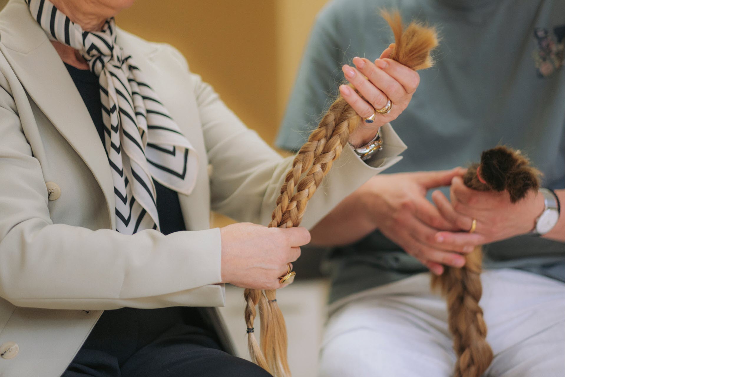 Zu sehen sind zwei Personen, die abgeschnittene Zöpfe in ihren Händen halten. 
