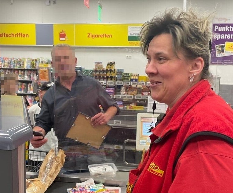 Eine Frau sitzt an einer Supermarktkasse und lächelt. 