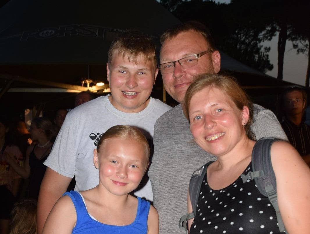 Eine Familie lächelt für ein Foto. Hinten steht ein Junge mit dem Vater, im Vordergrund ein Mädchen und die Mutter 