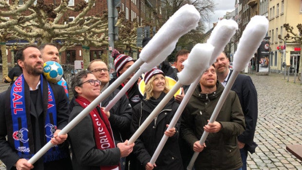 Eine Gruppe von Menschen hält große Wattestäbchen in die Luft