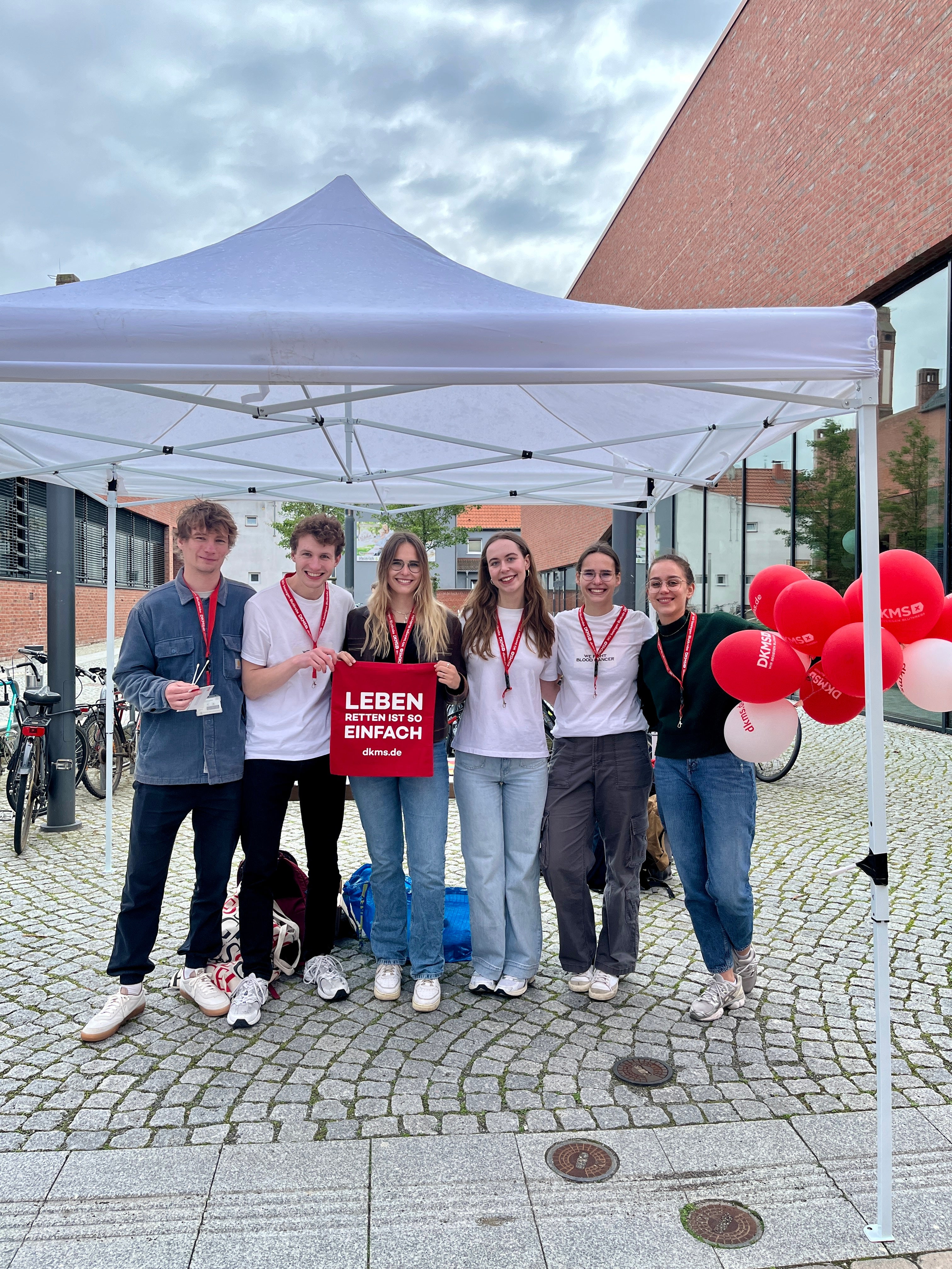Eine Gruppe von Menschen unter einem Zelt mit DKMS Merch in der Hand 