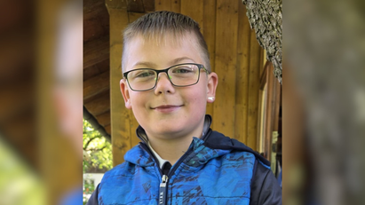 Ein Junge trägt eine Brille und eine blaue Jacke. 
