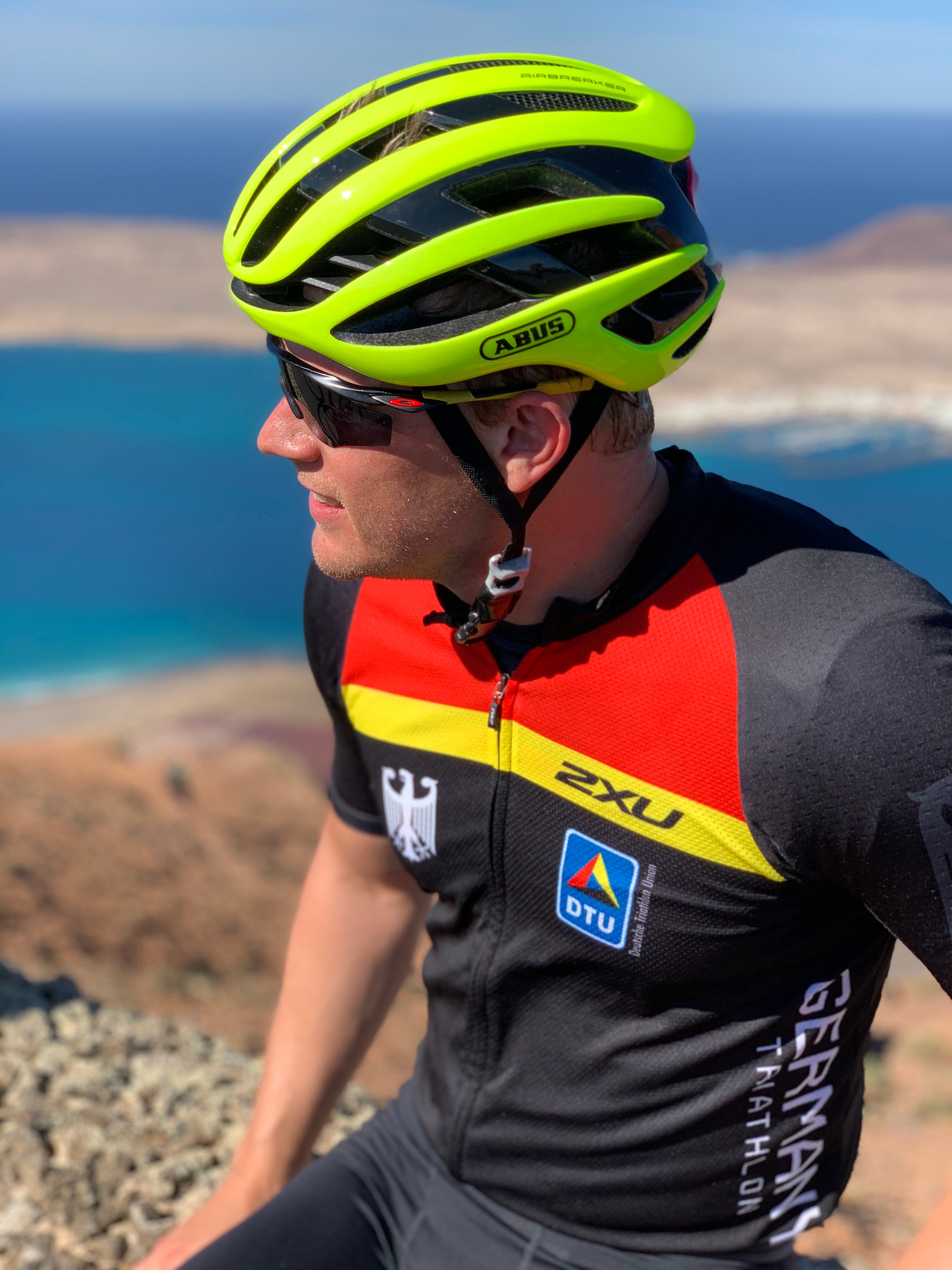 Ein Mann mit einem Helm und einer Sonnenbrille, im Hintergrund sieht man das Meer