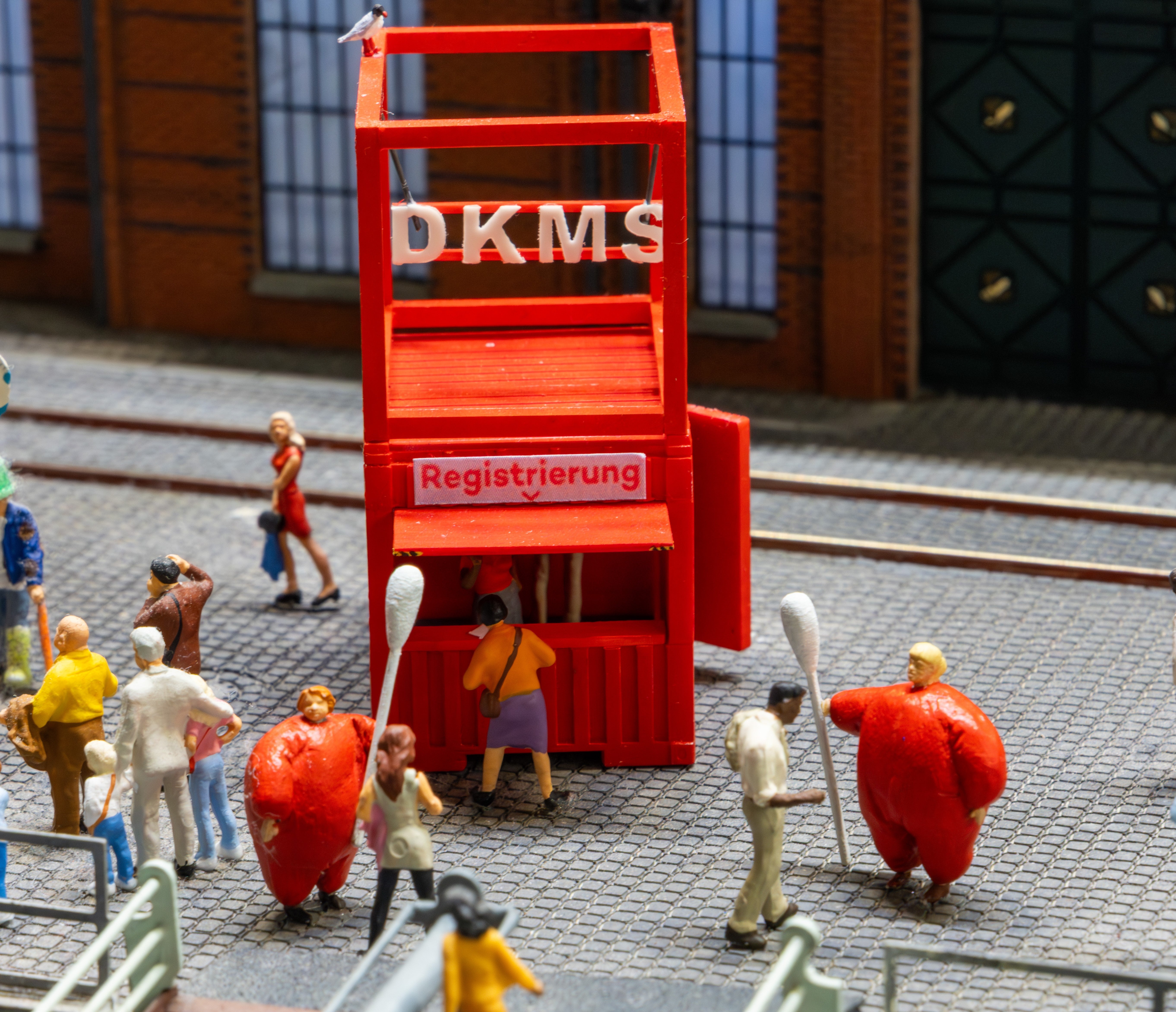 Eine Miniatur einer DKMS Registrierungsaktion. Zwei Figuren in roten Kostümen halten große Wattestäbchen.