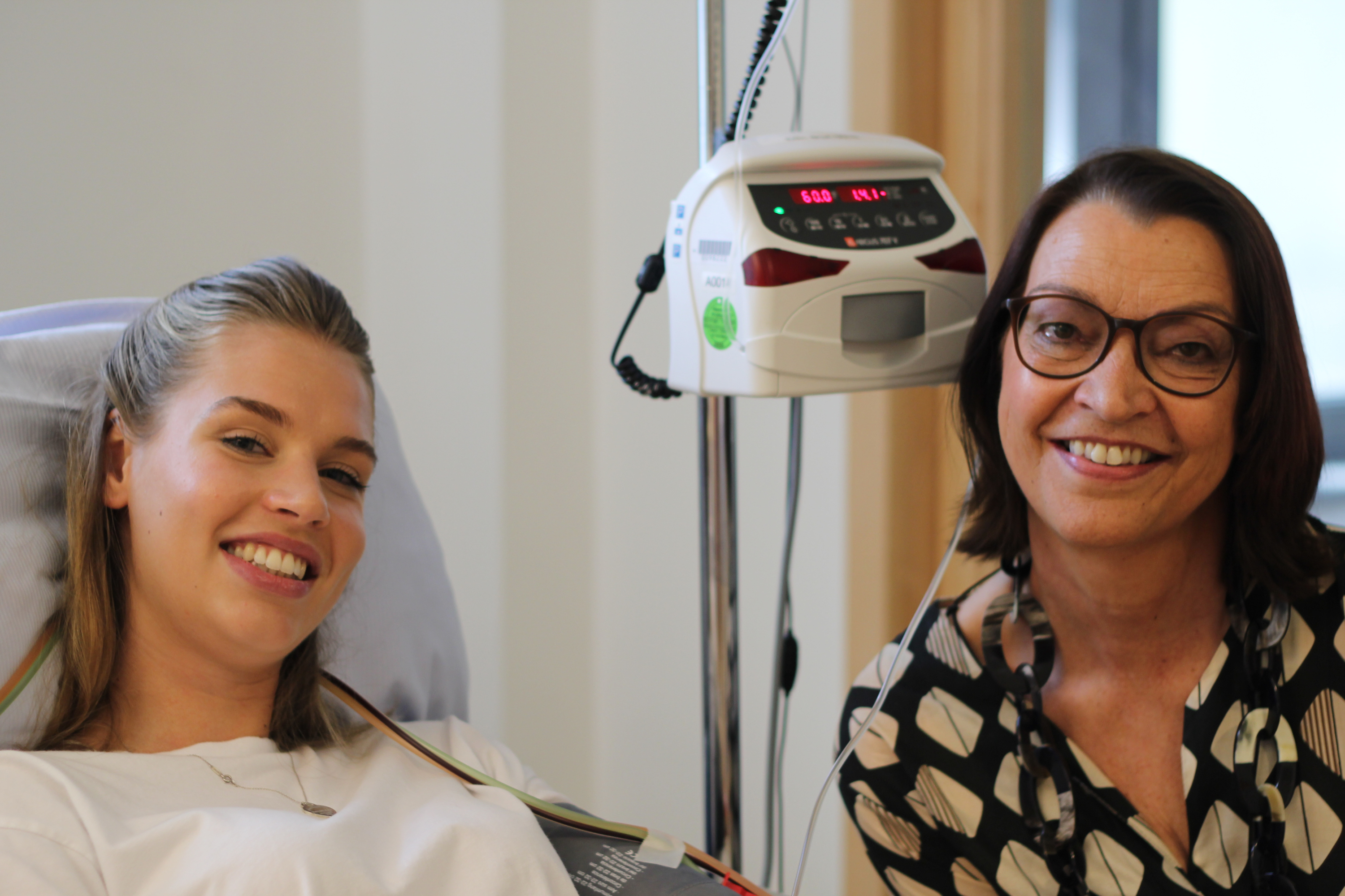 Eine Frau lächelt neben einer Frau in einem Krankenhausbett