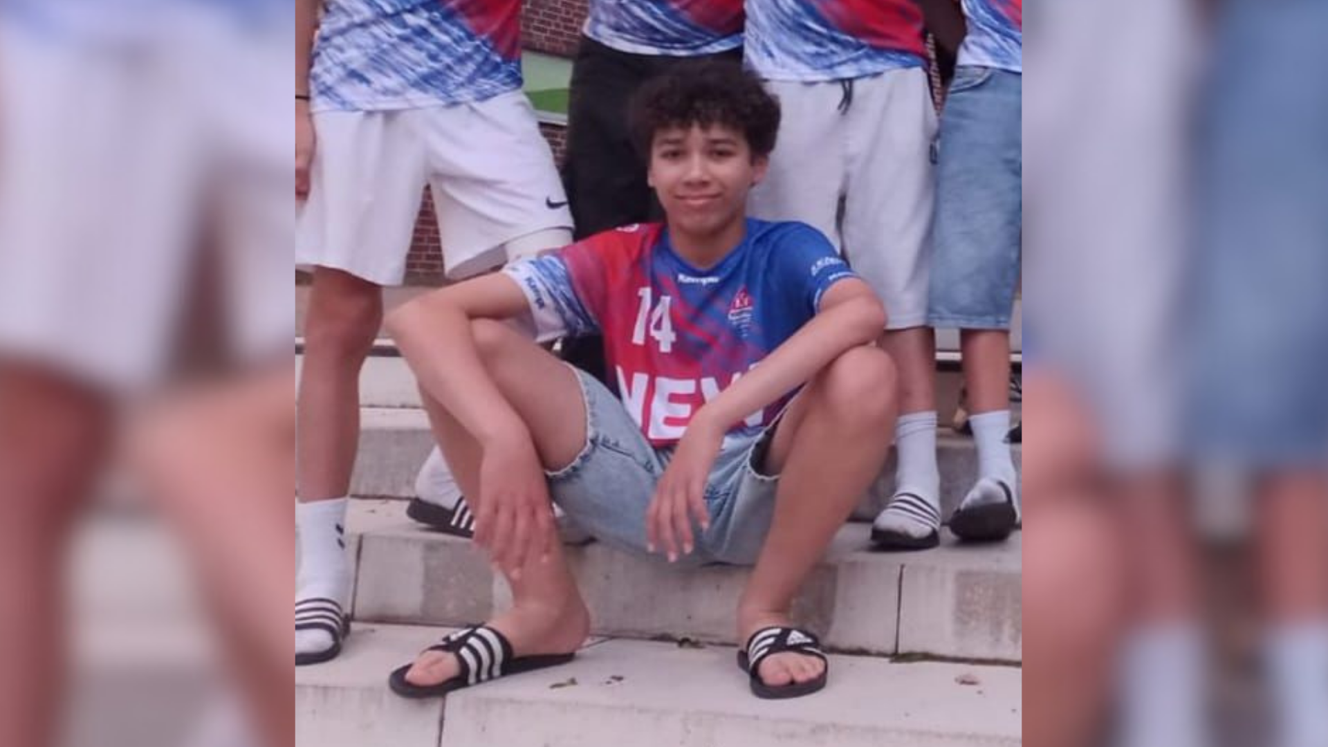 Ein Junge sitzt auf einer Treppenstufe und trägt ein Sportjersey. 