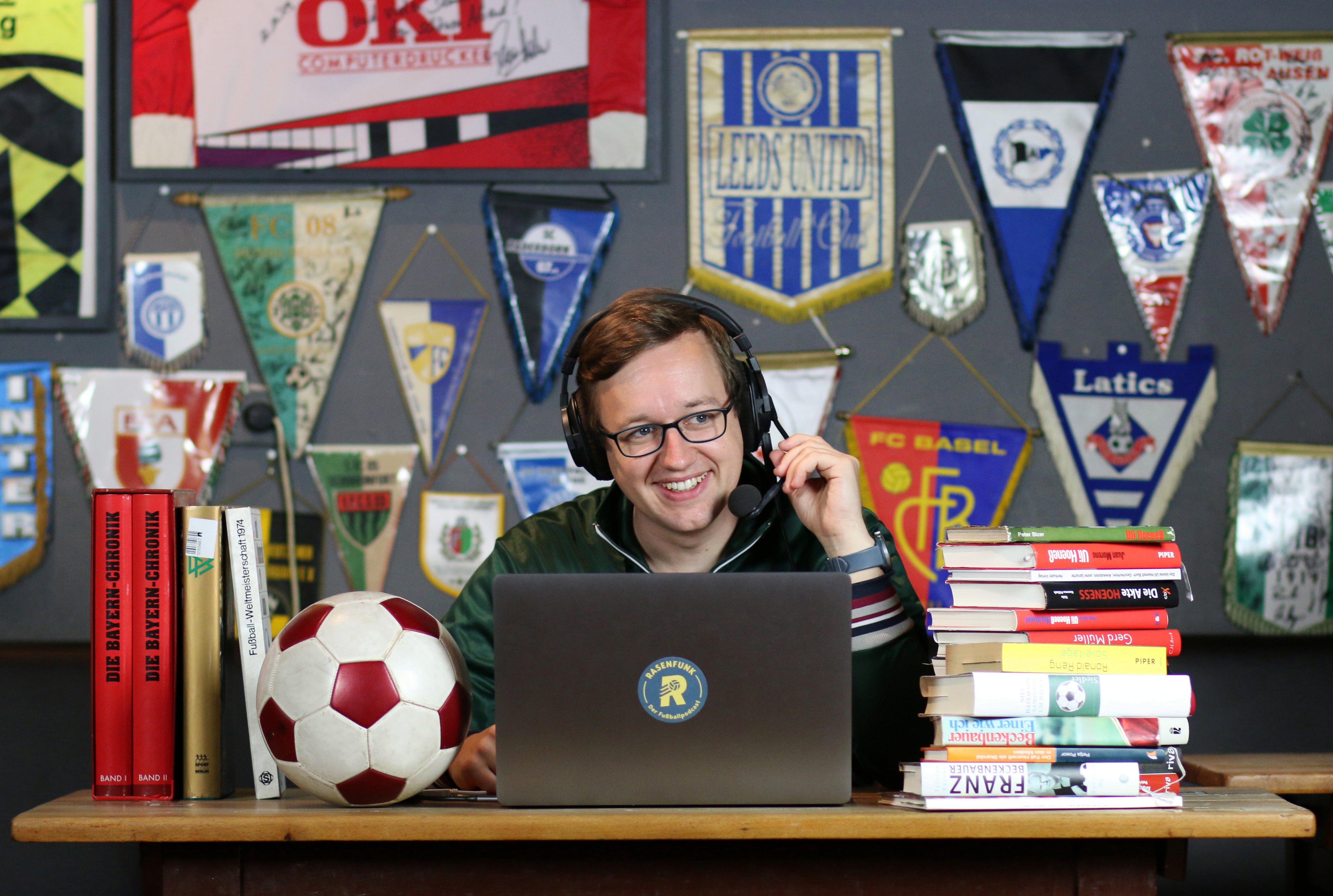 Ein Mann sitzt an einem Schreibtisch mit einem Laptop und einem Fußball