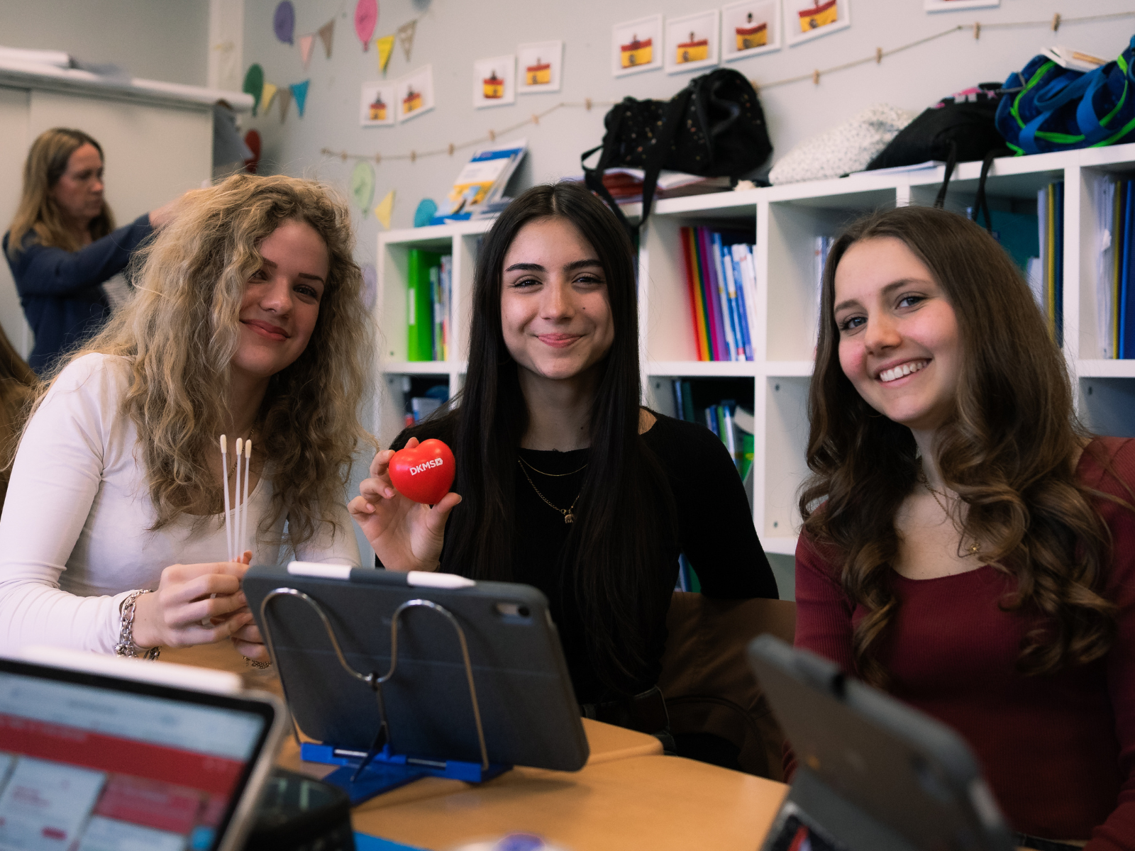 Drei Schülerinnen sitzen im Klassenraum und halten Wattestäbchen für den Wangenabstrich in der Hand