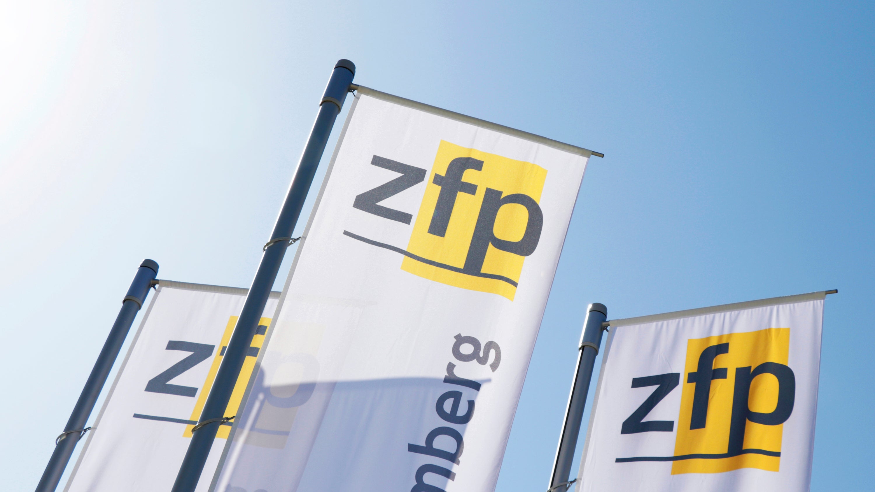 Drei Fahnen mit dem Zfp Logo vor einem blauen Himmel