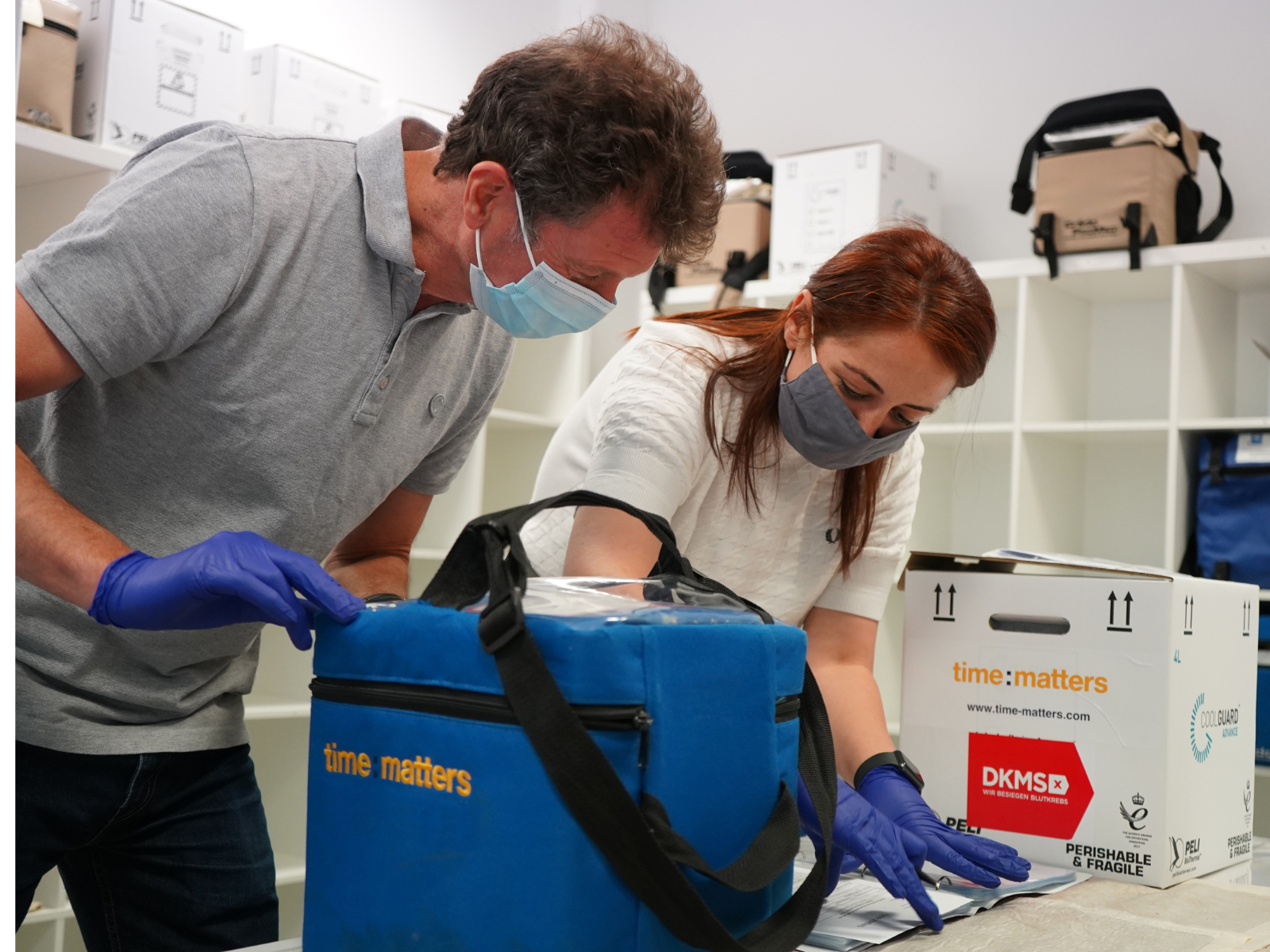 Foto von zwei Mitarbeiterinnnen - einer nimmt Stammzellen in einer Transportbox entgegen, die andere dokumentiert den Prozess