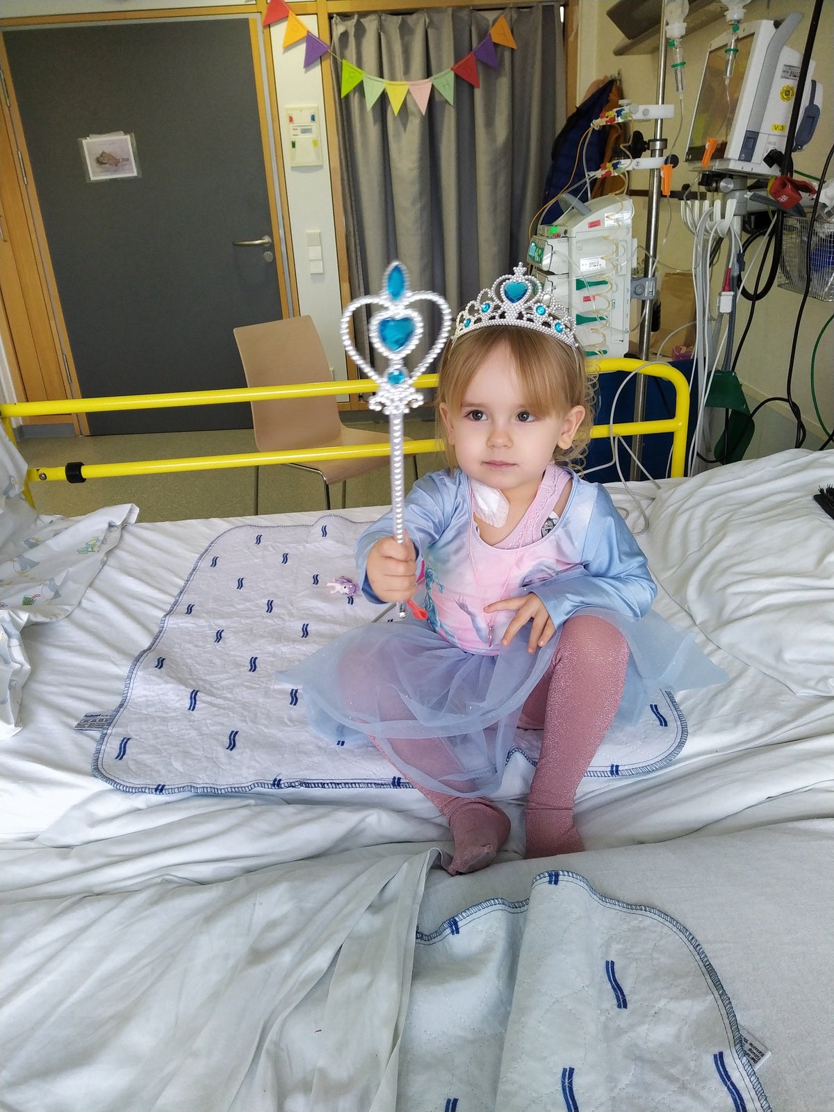 Ein Mädchen in einem Prinzessinnen-Kleid und Krone, sitzt auf einem Krankenhausbett 