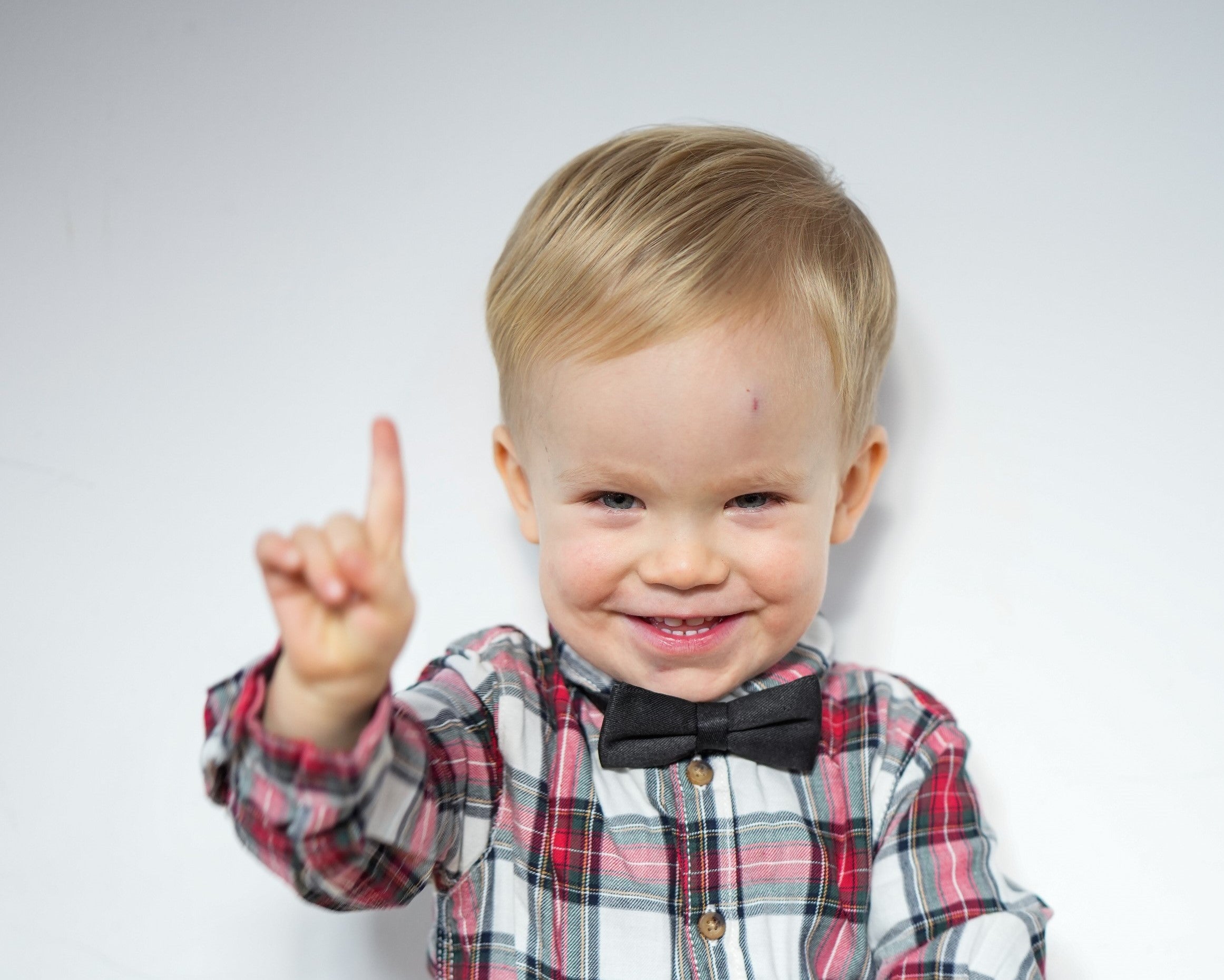 ein kleiner Junge lacht in die Kamera und hält seinen Zeigefinger hoch