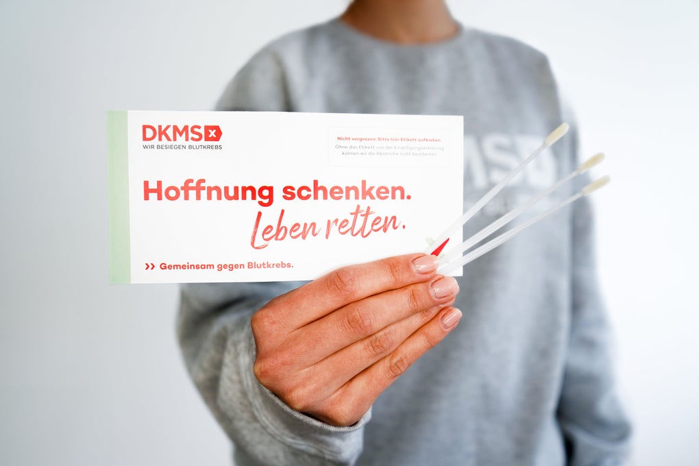 Eine Person hält eine DKMS-Klappkarte und drei Wattestäbchen in der Hand.