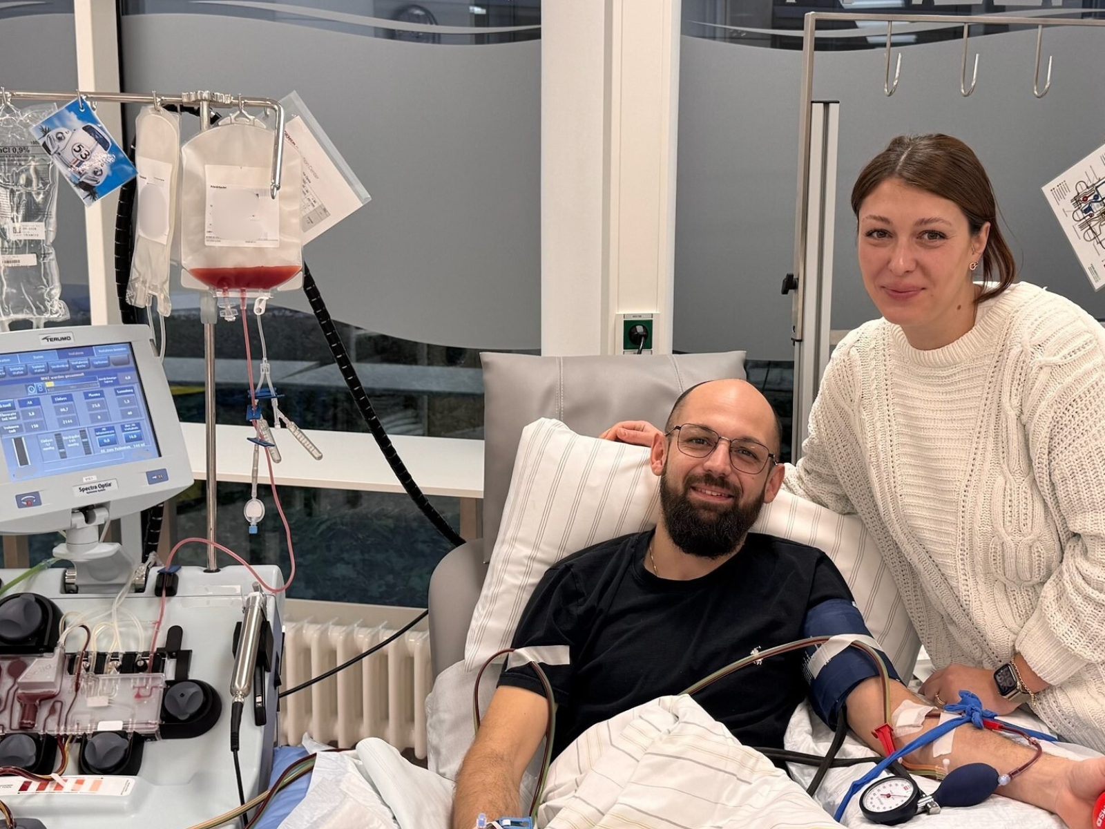 Pascal liegt in einem Krankenhausbett während der Stammzellenspende, Marie steht neben ihm