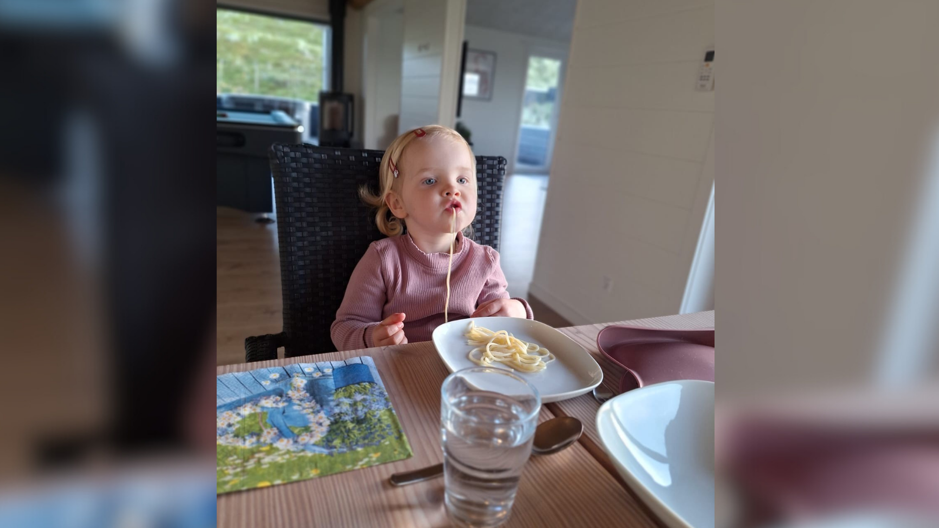 Ein kleines Mädchen sitzt an einem Tisch und isst Spaghetti.