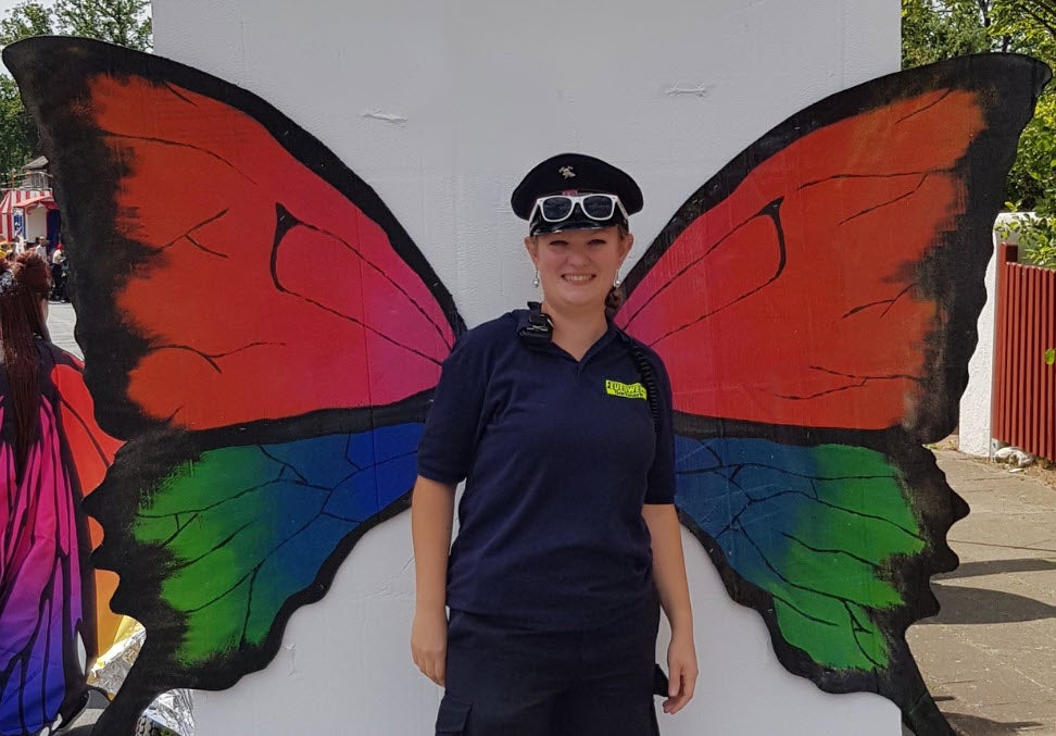 Katrin steht vor einer weißen Wand, auf der Schmetterlingsflügel abgebildet sind