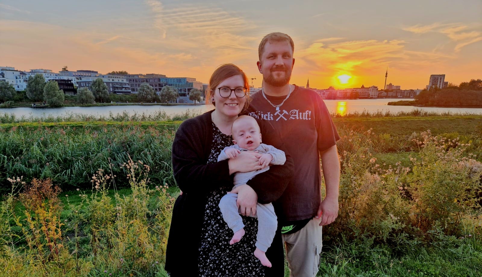 Ein Mann und eine Frau halten ein Baby vor einem Sonnenuntergang