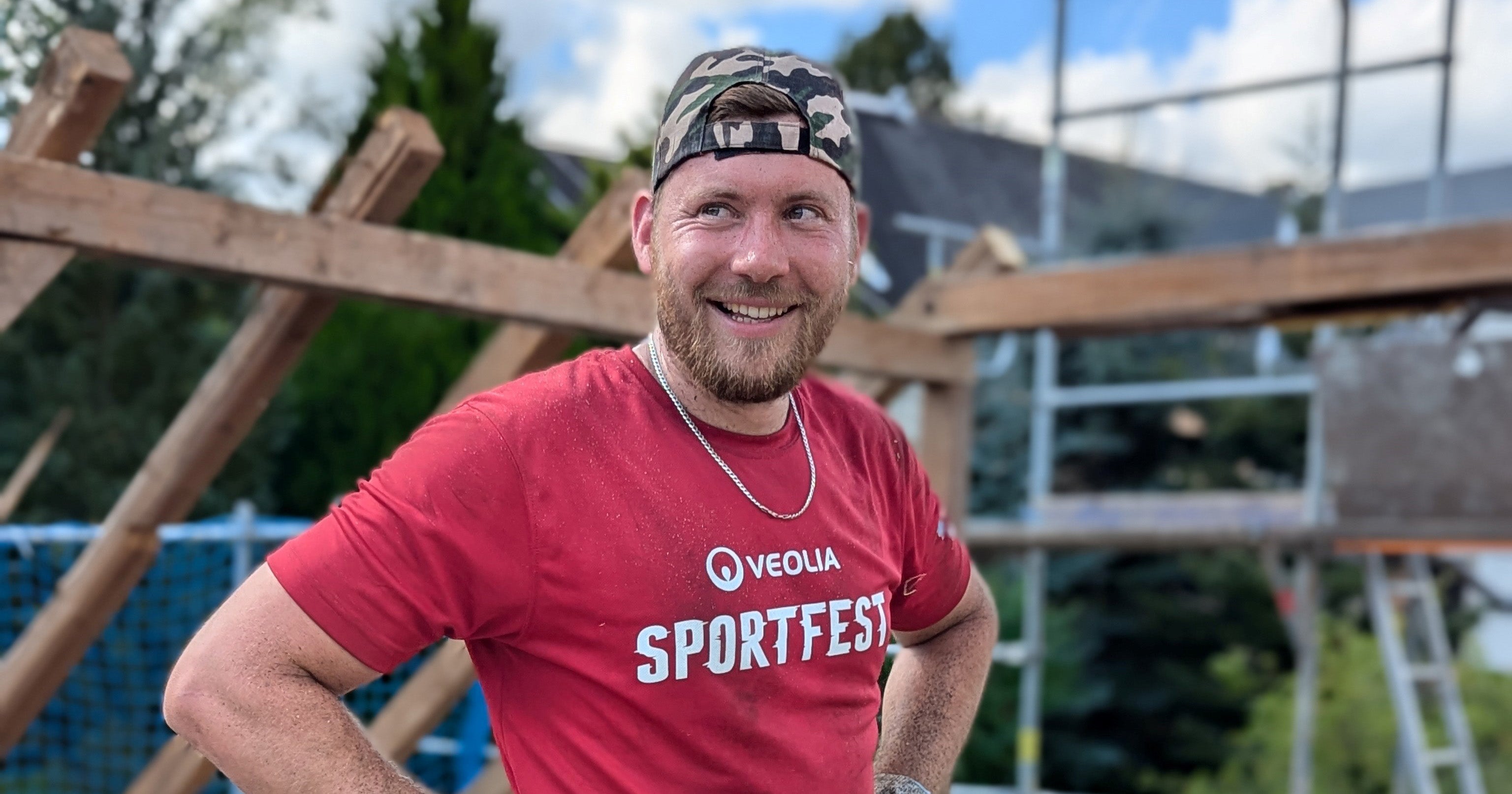 Ein Mann steht vor einem Baugerüst im roten T-Shirt und mit einem Kopfbedeckung.