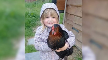 Ein junges Mädchen hält ein Huhn auf dem Arm und lächelt in die Kamera.