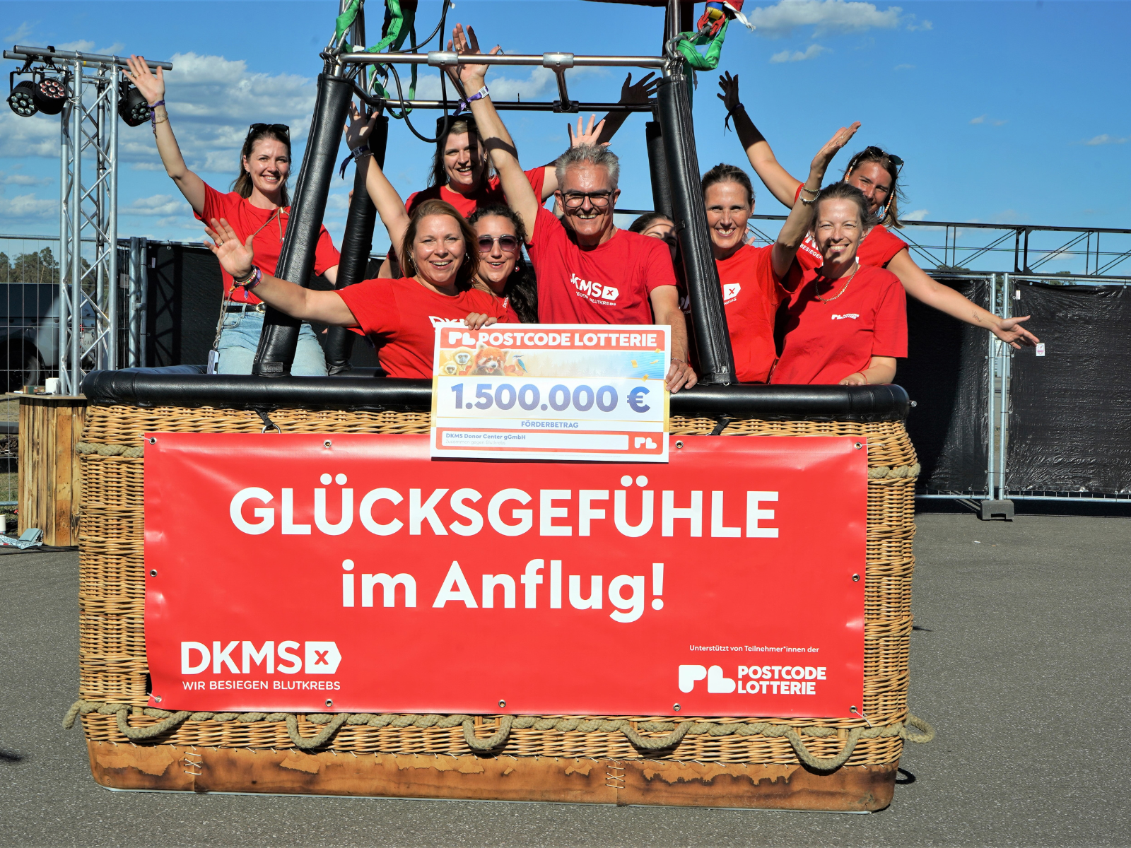 Das DKMS Team hält den Scheck von Postcode hoch, während es im Korb eines Heißluftballons steht