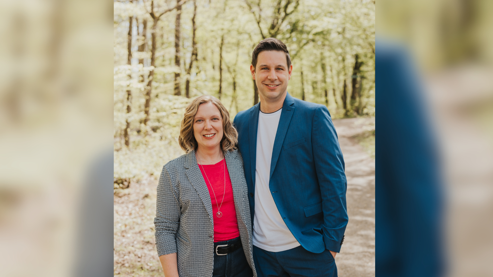 Eine Frau und ein Mann stehen Arm in Arm in einem Wald. 