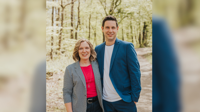 Eine Frau und ein Mann stehen Arm in Arm in einem Wald. 