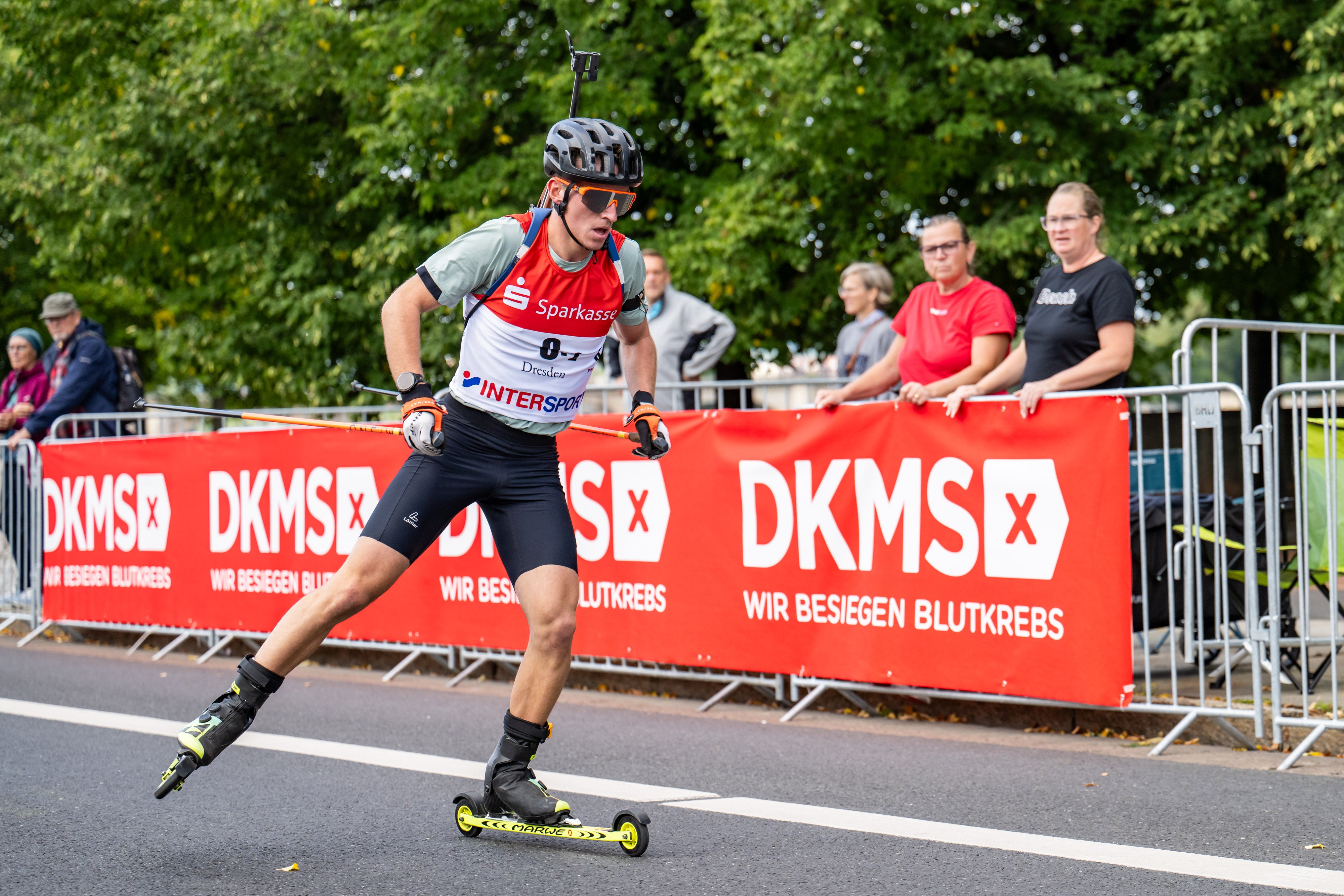 Ein Biathlon-Athlet auf rollenden Skiern vor dem Banner der DKMS.
