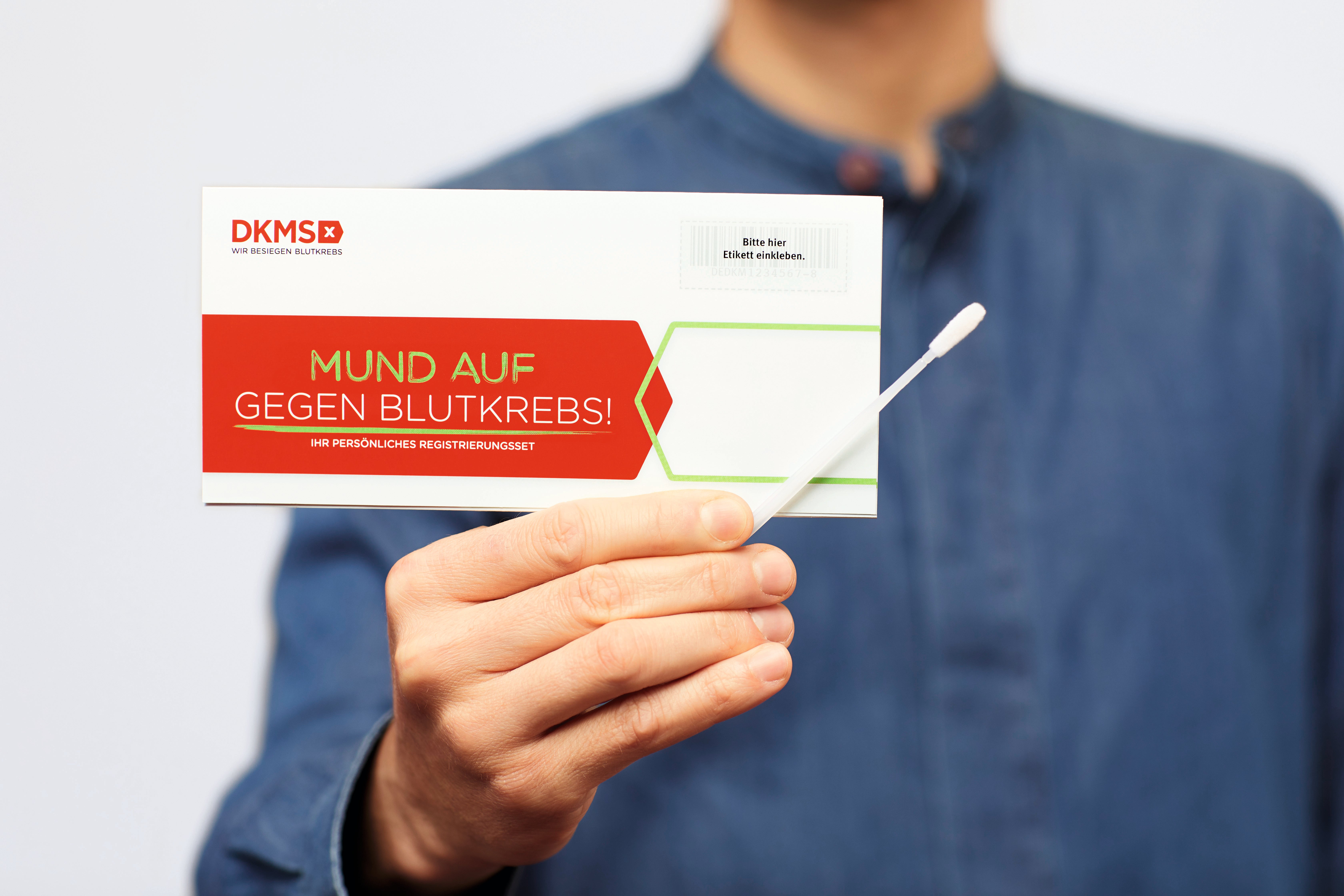 Eine Person mit einer Karte von der DKMS und einem Wattestäbchen in der Hand