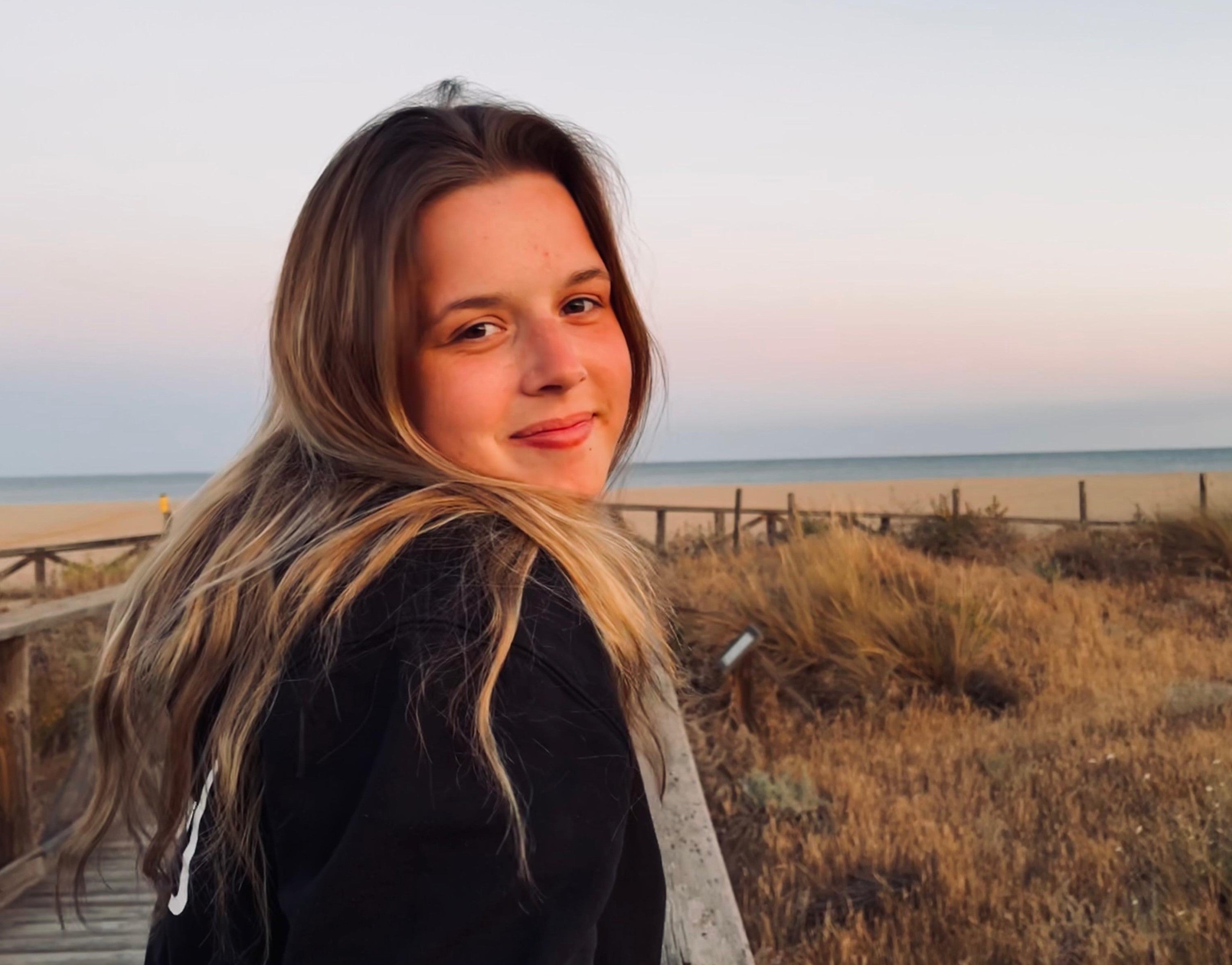 Julia steht am Strand und lächelt in die Kamera.