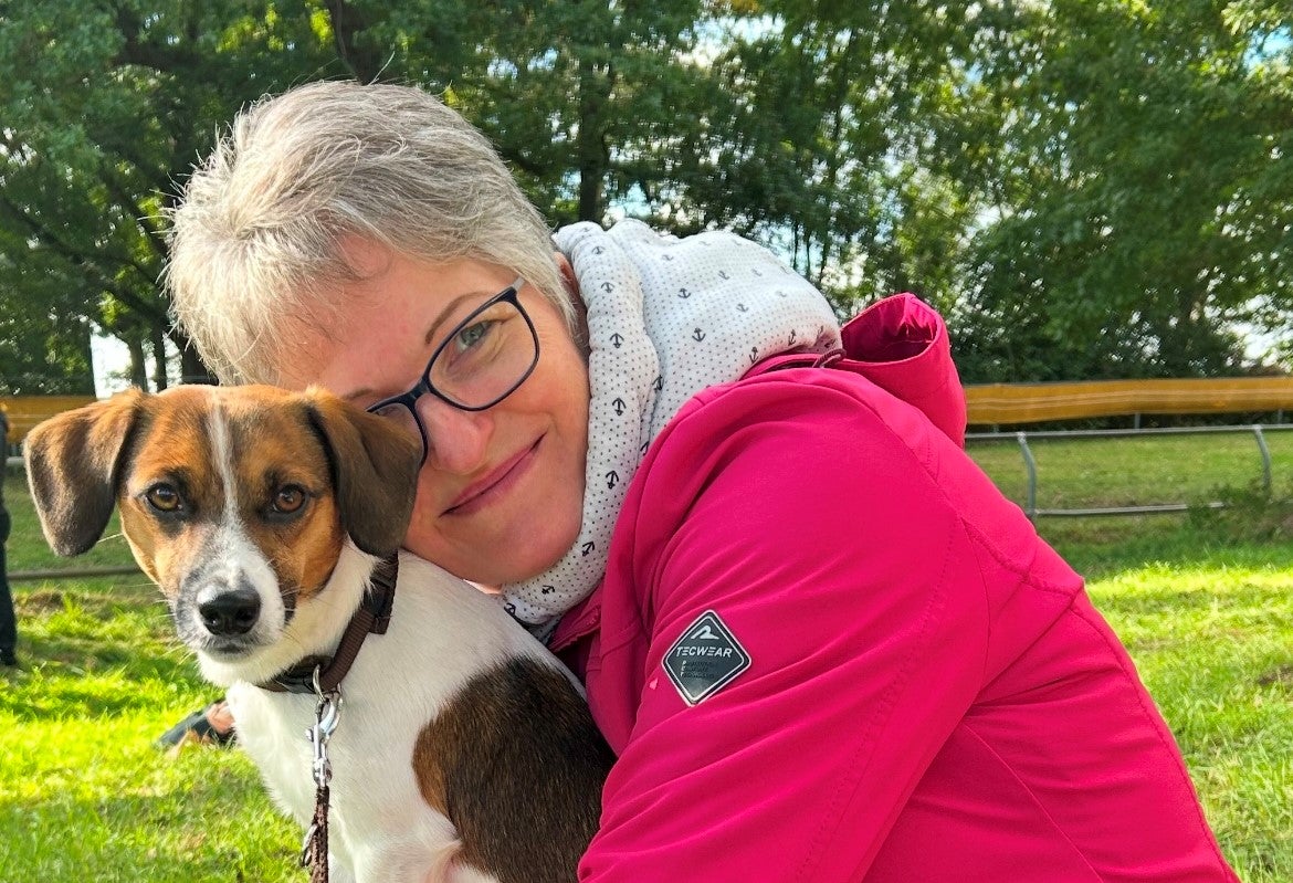 Eine Frau hält einen Hund, im Hintergrund sieht man einen Park