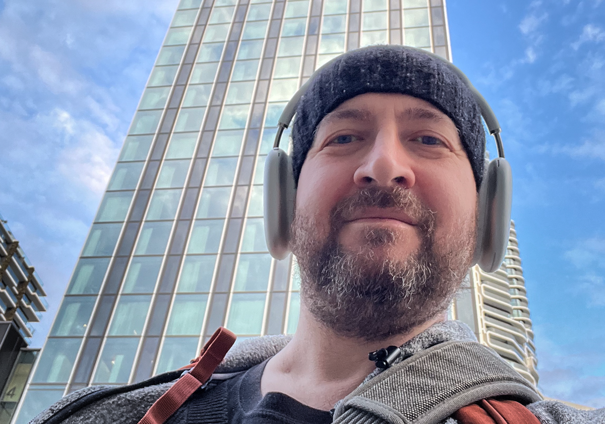 Ein Mann mit Kopfhörern und einer Mütze steht vor einem Hochhaus