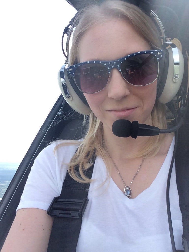 Eine Frau sitzt in einem Helikopter und trägt ein Headset und eine Sonnenbrille 