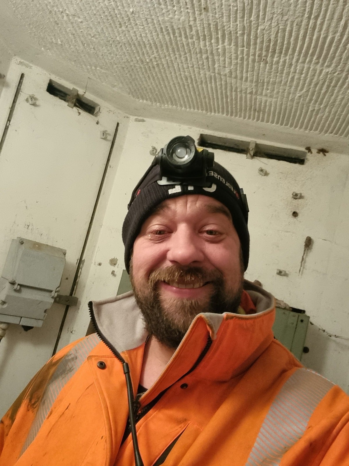 ein Mann macht ein Selfie in Arbeitskleidung, er hat eine Stirnlampe auf
