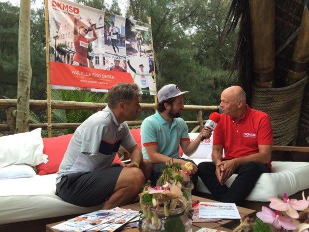 Zwei Männern sitzen auf einer Couch und interviewen einen dritten Mann. Dieser trägt ein rotes DKMS T-Shirt